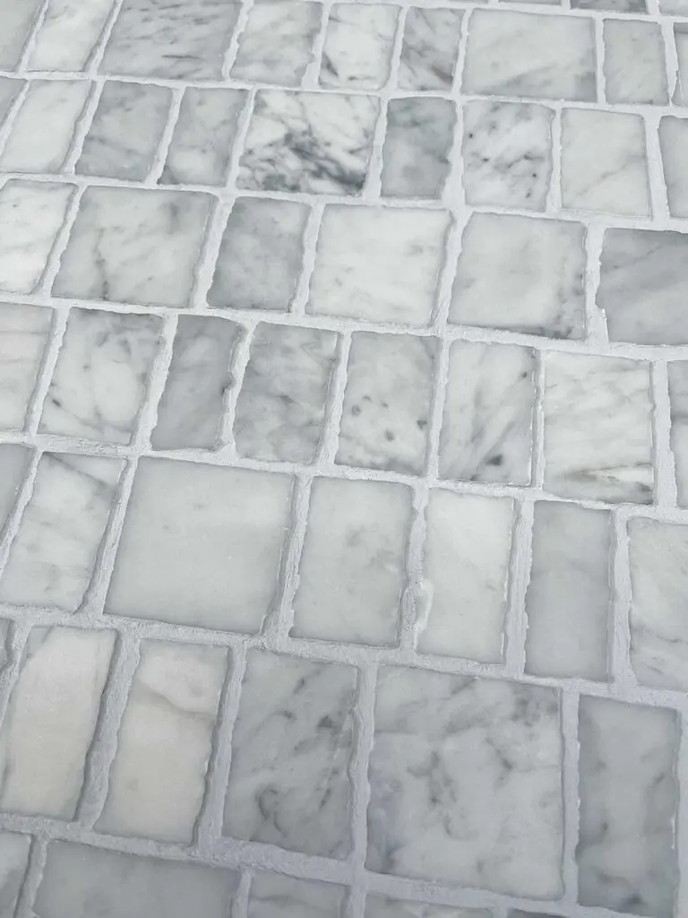 Närbild av marmormosaik med huggna kanter i Carrara marmor och ljusgrå fog