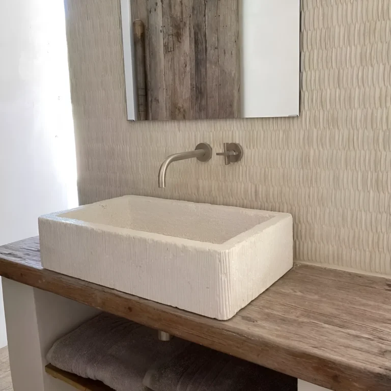 badrum med handfat i krämfärgad kalksten och keramikmosaik
