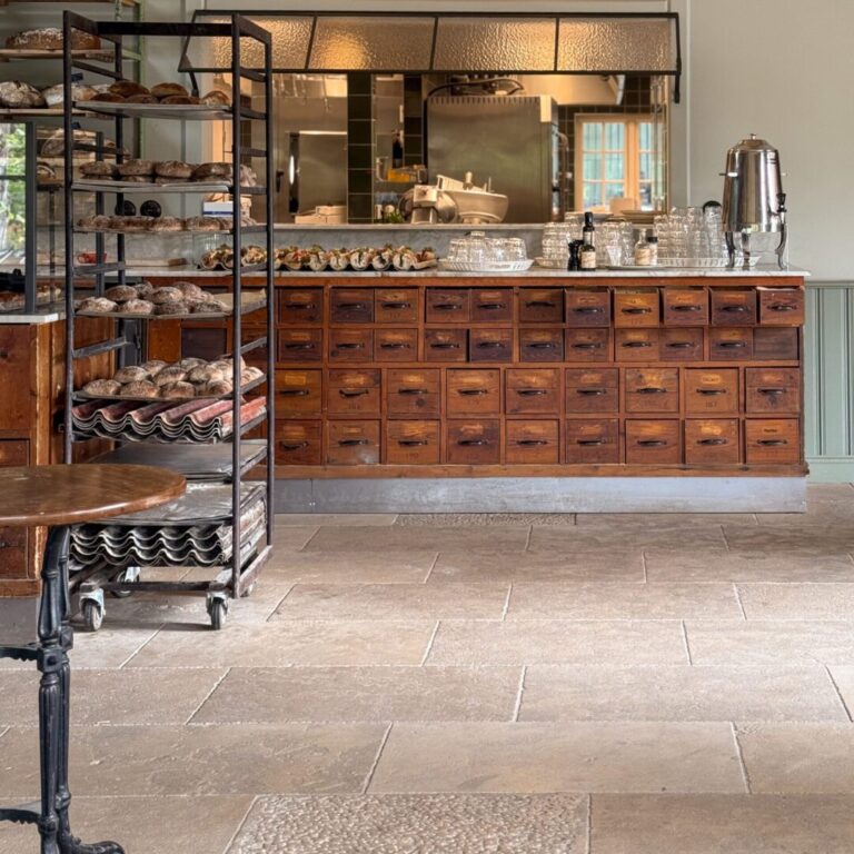 Café med en köpmannabänk i trä och en vagn med nybakat bröd, inrett med antikbehandlad kalksten för en rustik känsla.