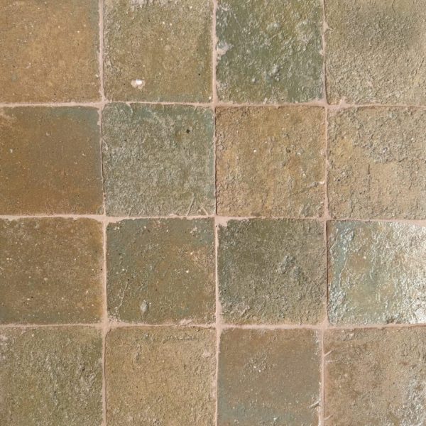 närbild av ett glaserat tegelgolv med gröna och beiga nyanser som skapar en livfull atmosfär.