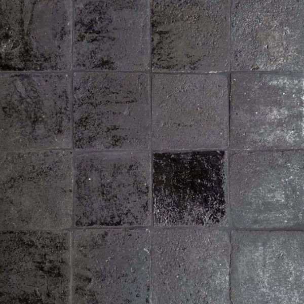 närbild av ett glaserat tegelgolv med nyanser i svart som skapar en livfull atmosfär.