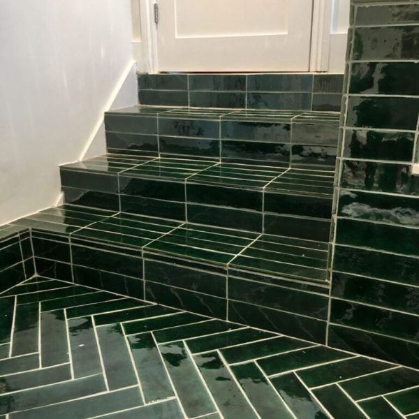 mörkgrönt handgjort kakel lagt i fiskbensmönster på golv och i trappa