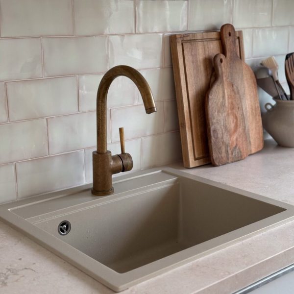 krämfärgat kakel på en vägg i ett kök, mässingsblandare och trädetaljer