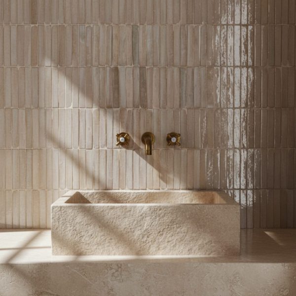 rustikt badrum med mässingkran, massiv vask i ljus kalksten och smala zellige-kakel i neutrala toner