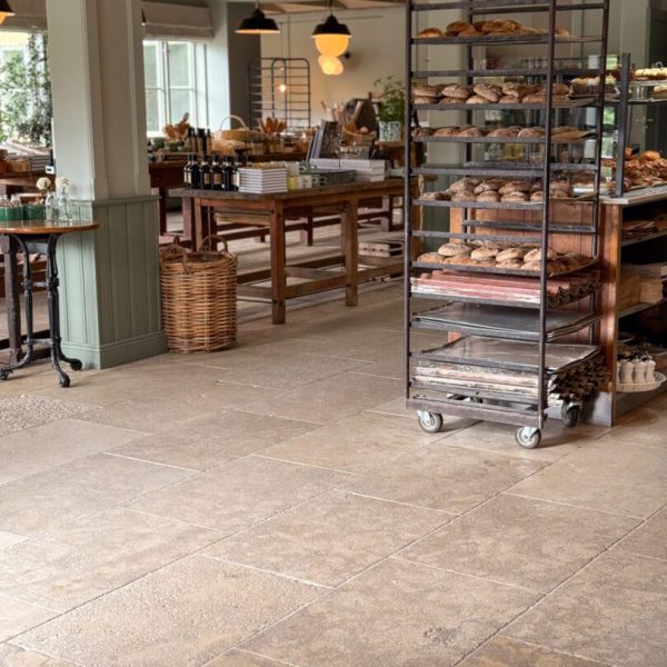 Stort café med en köpmannabänk och ett stort träbord, inrett med antikbehandlad kalksten för en rustik känsla.