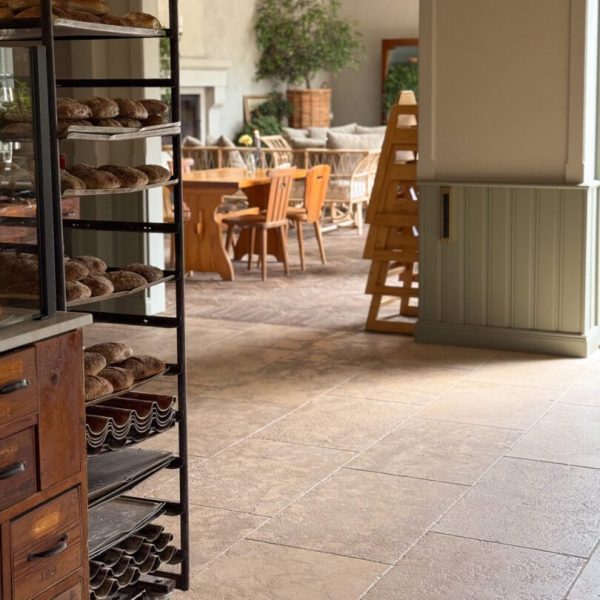 Stort café med en köpmannabänk och ett stort träbord, inrett med antikbehandlad kalksten för en rustik känsla.