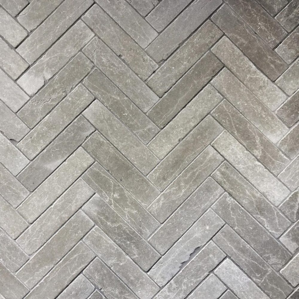 grå tumlad kalksten lagt i fiskbensmönster på golv