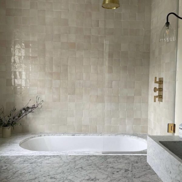 badrum med badkar täckt av marmor och väggarna täckta av ett krämigt zellige kakel